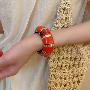 Detail of wide red acrylic and gold metal bangle bracelet on a model's wrist