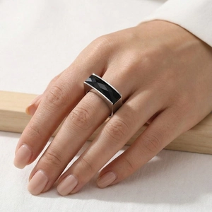 Macro detail of a silver ring featuring a rectangular faceted black gemstone on the finger
