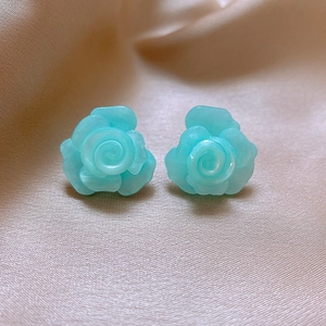 Detailed close-up of blue rose flower earrings on silk fabric with elegant petal texture