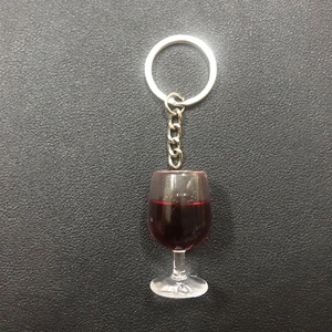 Close-up of a miniature resin red wine goblet keychain on black textured surface