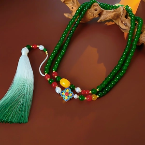 Detail of green beaded necklace featuring floral pendant and long gradient tassel fringe