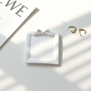 Detailed view of a white ceramic bow jewelry tray with golden earrings on a bright surface