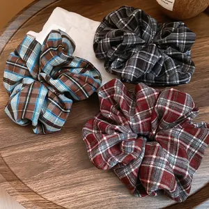 Three elegant plaid scrunchies in blue, black, and red patterns on a wooden tray