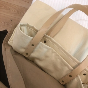 Detail of canvas tote bag showing durable leather handles with metal rivets and fine stitching
