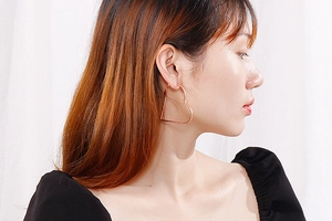 Close-up of a model wearing large rose gold heart-shaped hoop earrings on white background