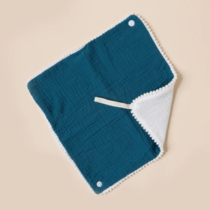 Detail of teal muslin baby bib showing soft cotton texture and white pom-pom trim