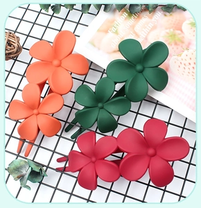 Detail of matte floral hair clips in orange, green, and red on a black grid display