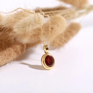 Detail shot of a 18k gold plated necklace with a ruby-red gemstone on a white surface