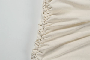 Detailed close-up of side ruched texture on elegant beige deep V bodycon dress