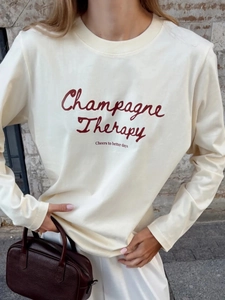Λεπτομέρεια στάμπας Champagne Therapy σε κρεμ βαμβακερή μπλούζα με μακριά μανίκια γυναικεία