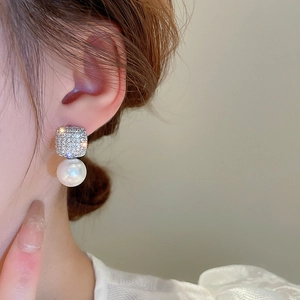 Close-up of elegant square zircon and large white pearl earrings worn by a model