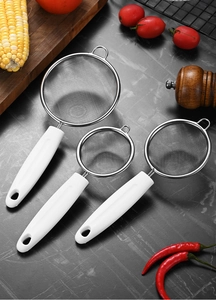 Three sizes of stainless steel kitchen strainers with white handles on a dark stone surface