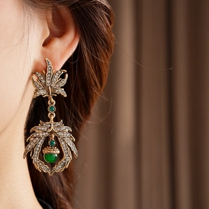Close-up of vintage gold leaf earrings with rhinestones and a green gem on a model