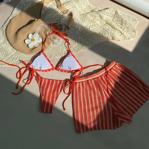 Detailed flat lay of striped three-piece bikini with crochet texture and resort accessories