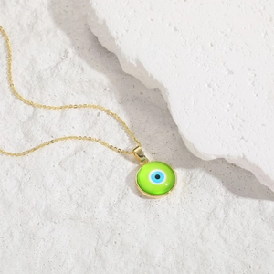 Macro detail of gold-plated evil eye pendant with green resin on a textured stone surface