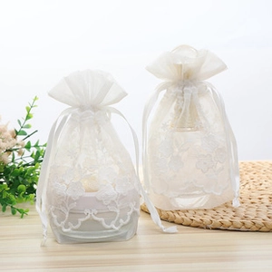 Detail showing two white floral embroidered organza drawstring bags on a wooden surface