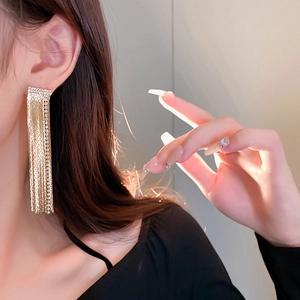 Close-up of elegant gold tassel earrings with square diamond accents worn by a model