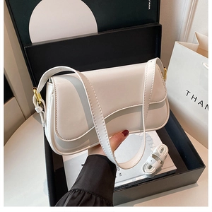 Detail view of white leather shoulder bag with gold hardware hooks inside a gift box
