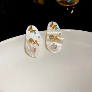 Boucles d'oreilles ovales en nacre avec papillon et rose dorés sur assiette en céramique