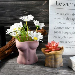 Macetas artísticas de torso humano en resina mate amarilla y rosa sobre mesa madera
