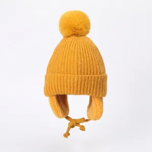 Close-up of yellow knitted winter hat for kids with soft fleece lining and fluffy pom-pom