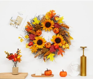 Close-up of autumn wreath with pumpkins, sunflowers, and maple leaves on a white wall