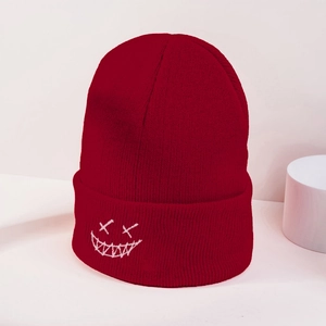 Detailed close-up of dark red knitted beanie with white embroidered ghost face design