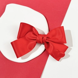 Detail der roten Satin-Schleifen-Haarspange mit kleinem Herzdekor auf weißer Keramik