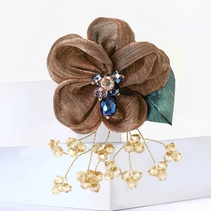 Close-up of brown lace flower brooch with blue bead core and golden tassel details
