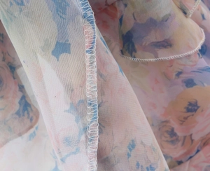 Close-up of floral chiffon fabric showing neat overlock stitching on the hem edge