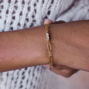Détail d'un bracelet gourmette en titane doré orné d'un zircon transparent porté au poignet