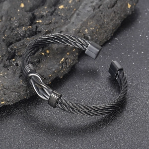 Macro shot of black twisted cable cuff bracelet resting on textured dark mineral stone