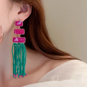 Detail of bohemian long tassel earrings with purple resin plates and green seed beads