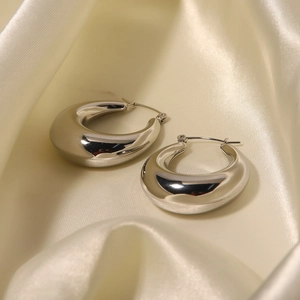 Detailed view of silver thick hoop earrings on soft cream silk with polished mirror finish