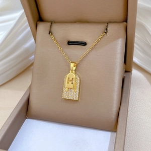 Macro detail of golden H-letter pendant with zircon stones on silk jewelry display