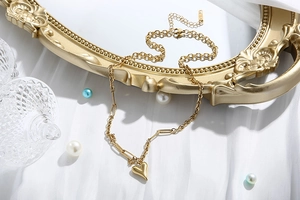 Dettaglio di una collana a doppio strato con ciondolo a cuore dorato su tessuto bianco