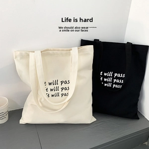 Nahaufnahme minimalistischer Canvas-Tragetaschen mit It will pass Aufdruck in Schwarz und Weiß