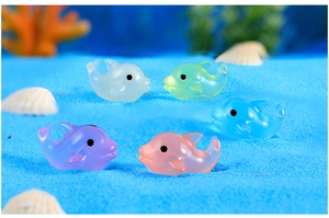 Close-up of five colorful resin mini dolphins on blue sand for moss micro-landscapes
