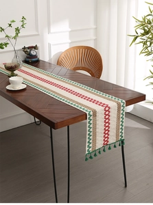 Detail of woven cotton table runner with orange geometric patterns and green tassels