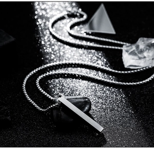 Macro shot of silver pillar pendant with box chain on dark textured stone