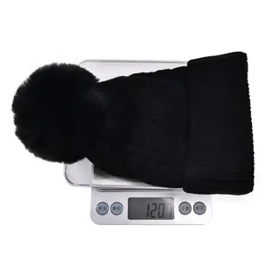 Detailed view of a black cable knit beanie with faux fur pom-pom on an electronic scale