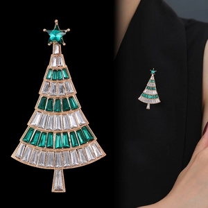 Golden Christmas tree brooch with green crystals and white zircons on a black garment