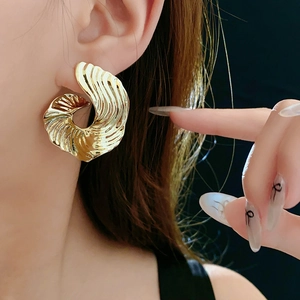 Close-up of gold swirl texture hoop earrings on model with high contrast lighting