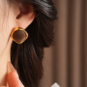 Détail de boucles d'oreilles carrées en métal doré et velours marron portées par mannequin