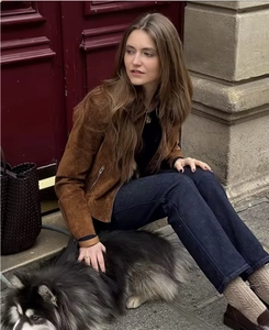 Outdoor shot of a brown suede jacket paired with dark denim jeans and a woven handbag