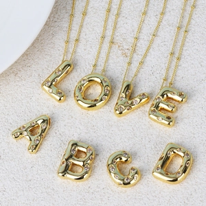 Gold hip hop initial necklace with sparkling diamonds on a beige stone surface