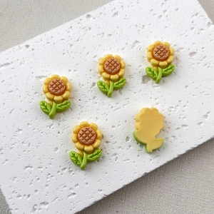 Flat lay of yellow resin sunflower charms with orange center and green leaves