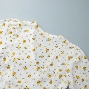 Détail d'une robe en coton blanc à imprimé floral jaune, manches bouffantes et texture