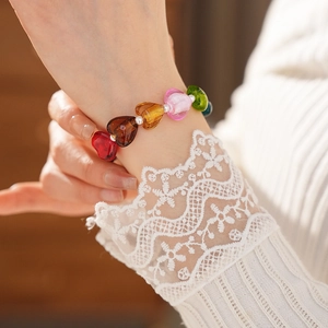 Close-up of heart-shaped glass pearls bracelet worn with a white lace sleeve