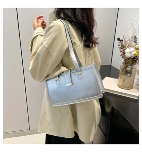 Detail of silver metallic underarm bag with square buckle worn by a model in a trench coat